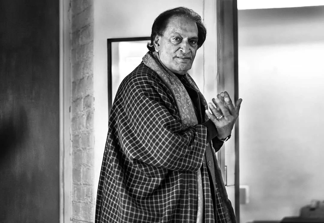 Black-and-white portrait of the photographer Raghu Rai in a checked shawl, gesturing as he speaks